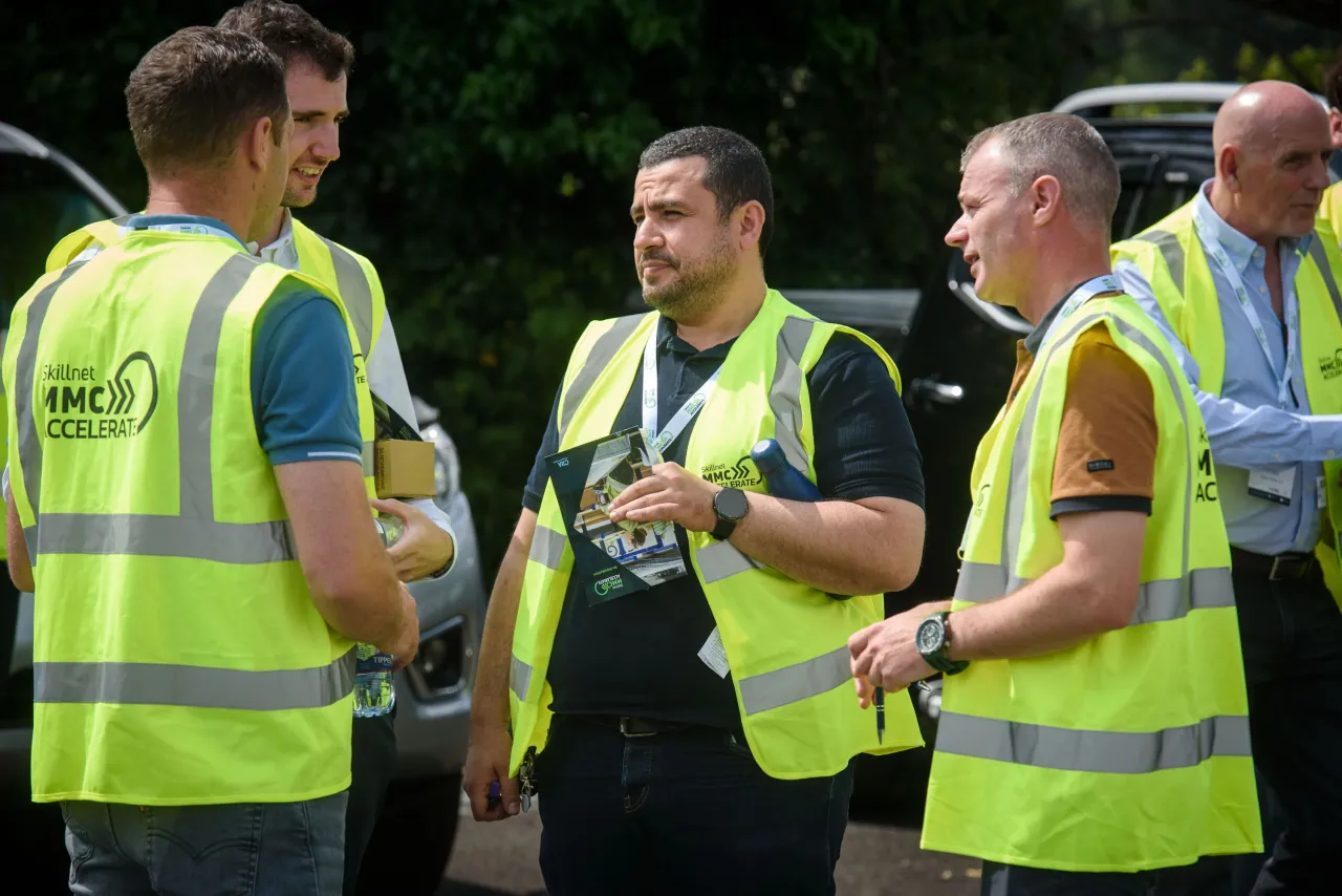 Four men in yellow high-visibility vests having a discussion outdoors.