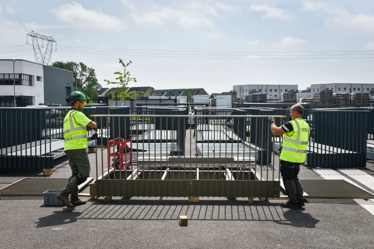Two workers in high-visibility jackets installing metal security gates outdoors.