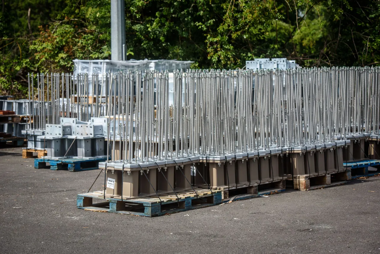 Rows of stacked metal scaffolding components on pallets in an outdoor storage area.