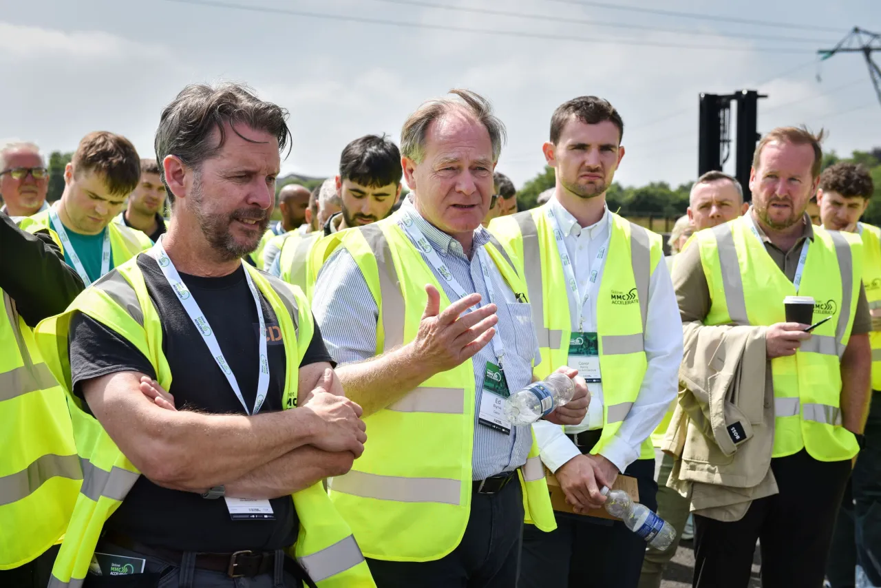 Group of men in yellow safety vests gathered outdoors at a construction or industrial site.
