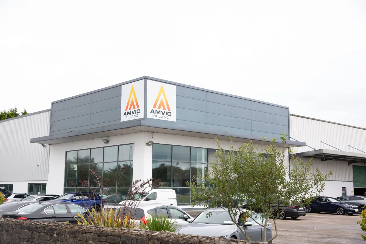 Modern commercial building with a yellow and gray logo, cars parked in front, overcast sky.