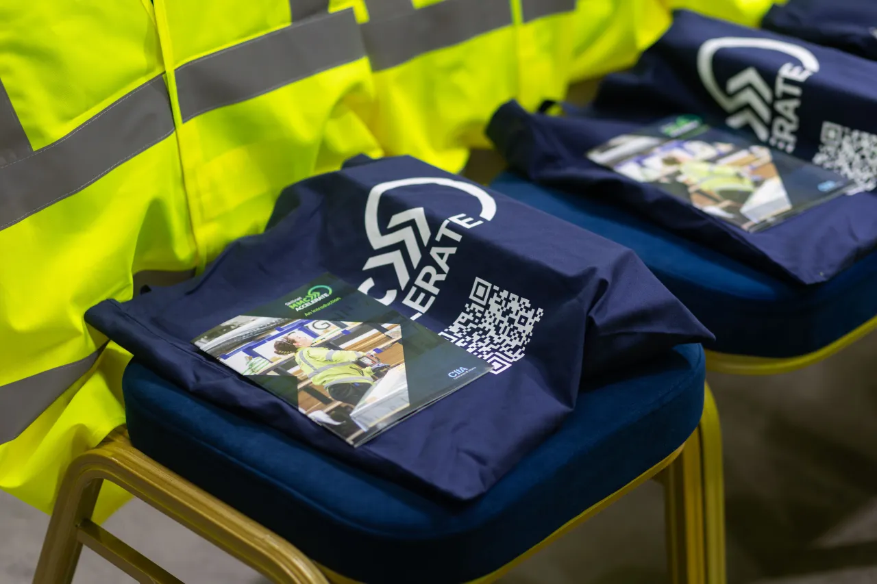 Navy blue folded t-shirts with QR code print, stacked on chairs beside a yellow high-visibility jacket.