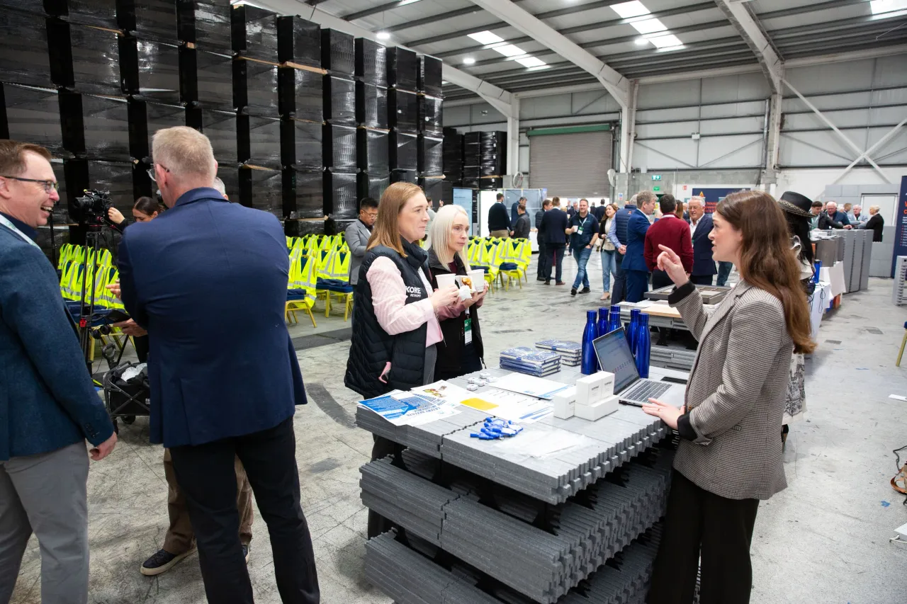 Business professionals in a large industrial warehouse, examining equipment displays during a facility tour.