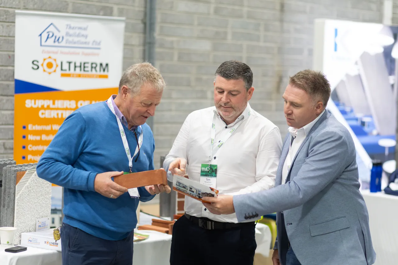 Three men in business casual attire reviewing documents at a trade show booth.