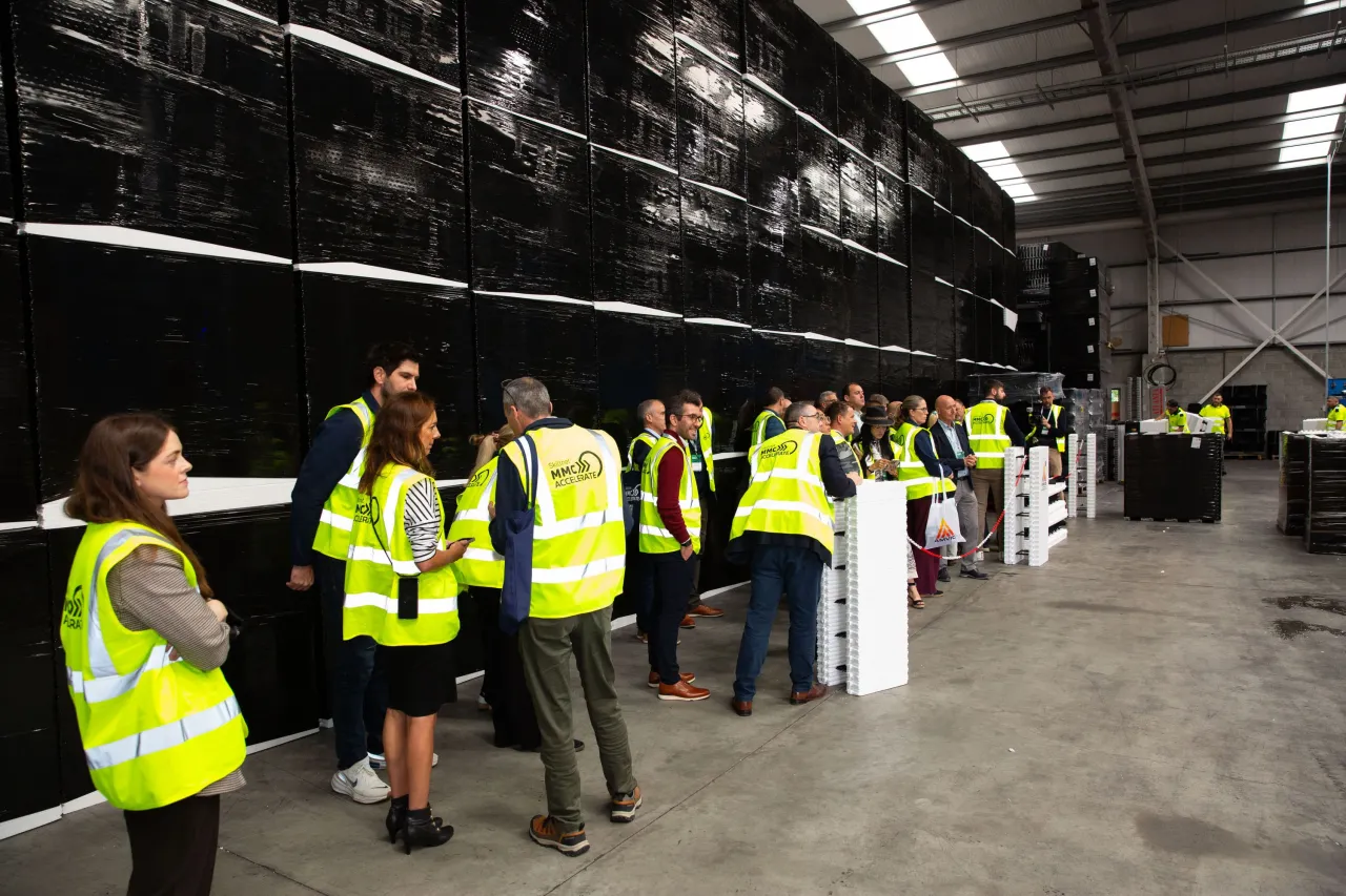 Group of visitors in yellow safety vests touring an industrial facility with large black machinery.