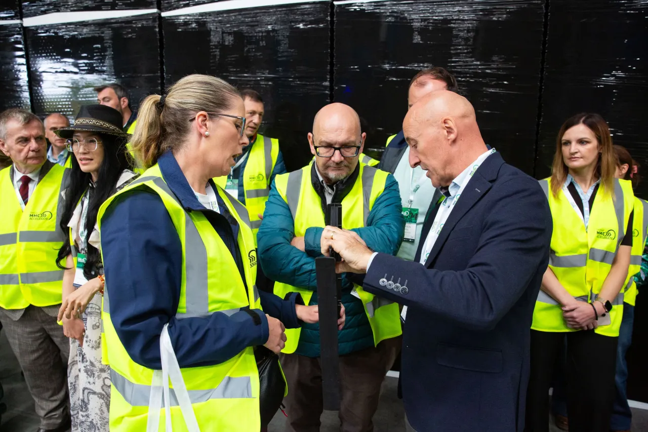 Two professionals in yellow safety vests engaged in conversation during a facility tour, surrounded by a group.