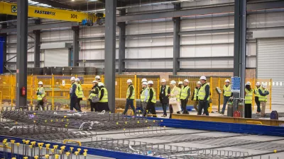 A group of people in high-vis jackets and white hard hats inspect a steel welding manufacturing facility.