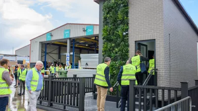 A group of people in high vis jackets enter a brick building one by one.