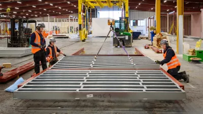 Three people in high vis vests inspect metal frames lying on the ground.