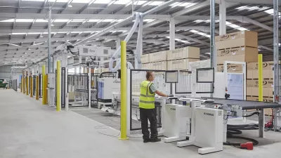 Person in high-vis vest operating a robotic system inside a construction manufacturing facility.