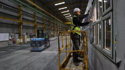 A male in a hard hat and high vis vest stands on a yellow scissor lift to test a window.