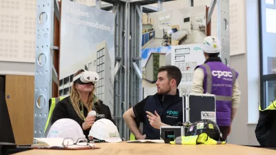 Two people sitting at a table, with the male watching as the female uses a VR headset.