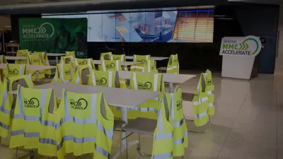High vis vests with the Skillnet MMC Accelerate logo hang off the back of white chairs around white tables in an event space with a screen in the background.