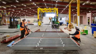 Three people in high vis vests and protective helmets inspect metal frames lying on the ground.