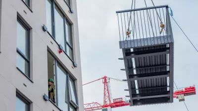 Prefabricated balcony being lifted by crane next to a multi-storey building under construction.