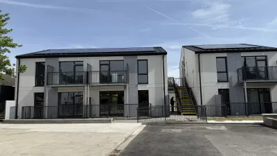 A row of modern houses with black metal balconies and black railings, and external steps running between them.