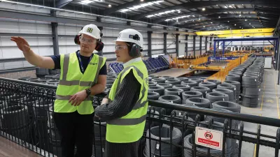 Two people wearing high vis jackets, hard hats and ear muffs, with one person pointing out something to the other.
