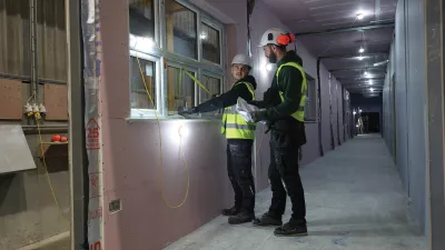 Two people in high-vis vests inspecting a window inside a construction unit