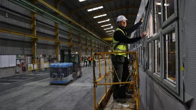 A male with a high vis vest and hard hat stands on a scissor lift to fit a window.