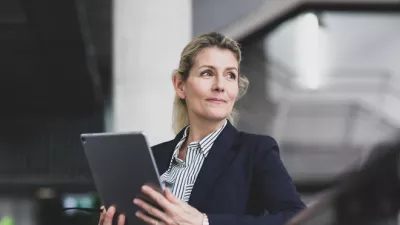 A female in a business suit holding a silver tablet.