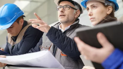 A group of people in hard hats review building plans on large paper charts.