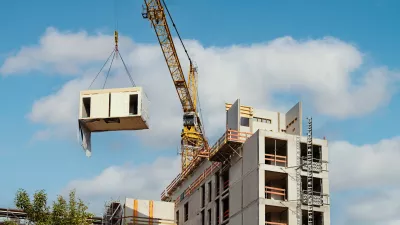A crane lifts a modular building unit across a construction site.