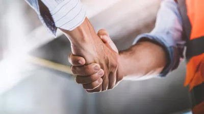 A person in a business shirt shakes hands with a person in a business shirt and high vis vest.