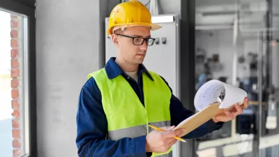 A male with a high vis vest, hard hat, and glasses reviews a chart on a clipboard.
