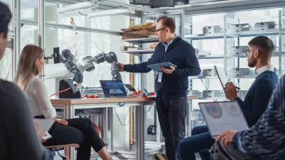 man displaying a robotic arm to a group of people in a classroom setting