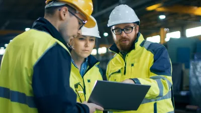A group of people in hard hats and high vis vests read from a tablet screen.