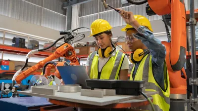 Two workers wearing high-visibility vests and hard hats are working with robotics.