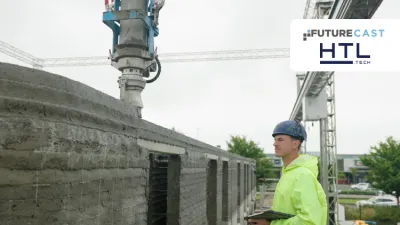 A construction worker in a hard hat and high-vis jacket observes a 3D printer building a concrete wall.