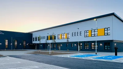 A modern two-storey school building with dark grey and white exterior panels, yellow accent features, and large windows.