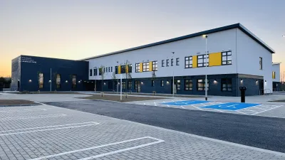 A modern two-storey school building with dark grey and white exterior panels, yellow accent features, and large windows.