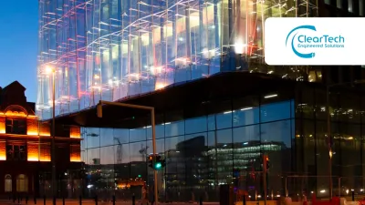 Modern glass building illuminated at night, reflecting lights and surrounded by urban street scene.