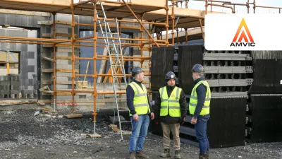 Three construction workers in helmets and safety vests discussing at a building site with scaffolding