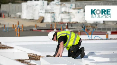 Construction worker in a high-visibility vest and hard hat installing insulation panels on a building site.