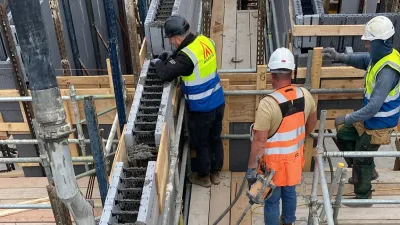Three construction workers in safety gear installing concrete into Amvic insulated concrete forms on scaffolding.