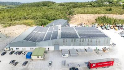 Industrial facility with large solar panels on the roof, surrounded by parked vehicles and storage materials.
