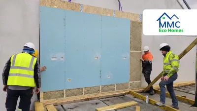 Workers in safety gear installing a large prefabricated wall panel on a construction site, with MMC Eco Homes logo in the corner.