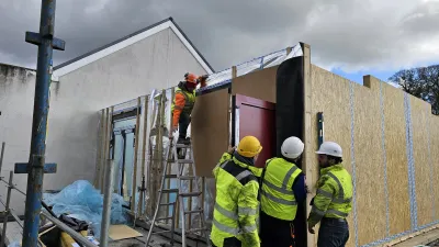 "Construction workers in safety gear installing large prefabricated wall panels,