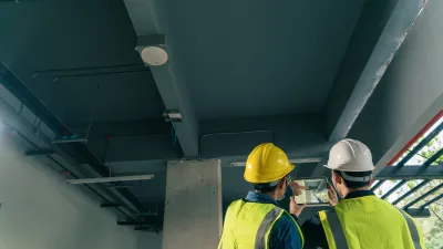 Two construction workers in safety vests and helmets inspecting ceiling installations