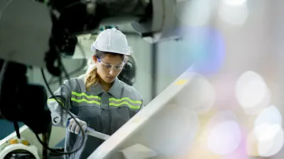 Person wearing a hard hat, safety glasses, and protective clothing operating equipment in an industrial setting.