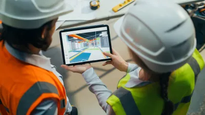 Two construction workers in hard hats review a BIM model of MEP services on a tablet at the jobsite.