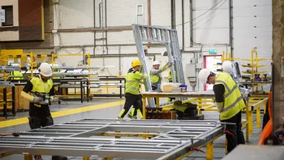 Construction workers in yellow safety vests assembling metal framing in a warehouse setting.