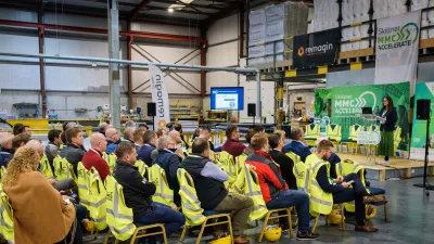 Audience seated in a factory setting wearing high-visibility vests, listening to a speaker presenting at the Skillnet MMC Accelerate event.