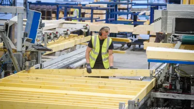 Worker in a high-visibility vest handling timber panels at an automated production line inside an offsite construction factory.