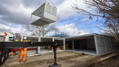 A modular building unit being lifted by a crane at a construction site.