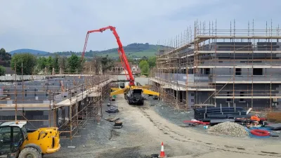 “Construction site with scaffolding, insulation formwork blocks, and heavy machinery operating between two rows of buildings.