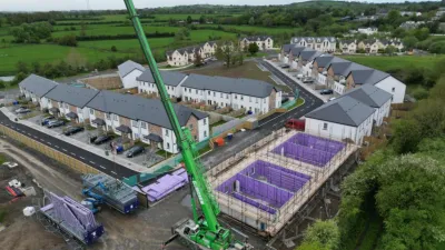 Aerial view of housing development under construction with a large green crane and purple foundation structures.